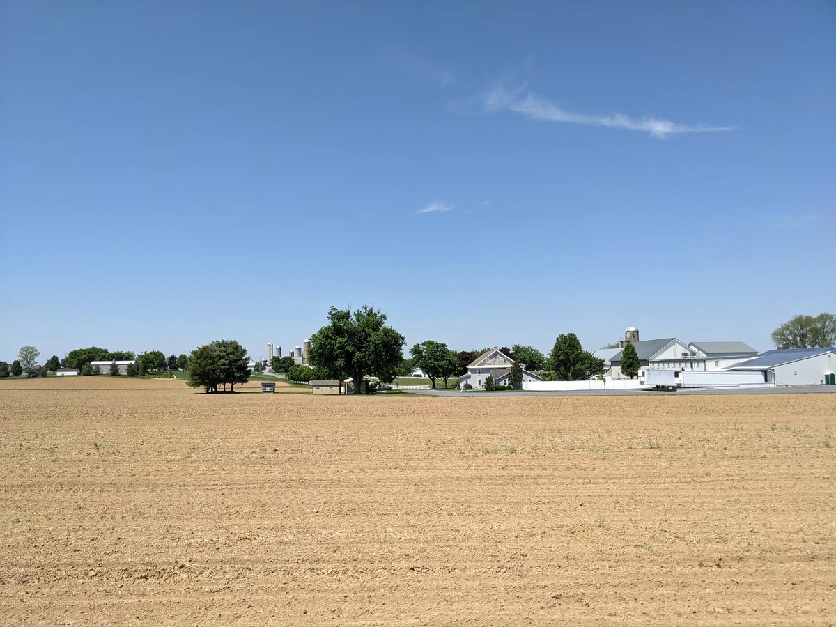 A clear sky over an empty field with a few farm buildings in the distance.